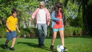 A joyful moment as a grandfather plays soccer with his grandchildren in a lush green park.